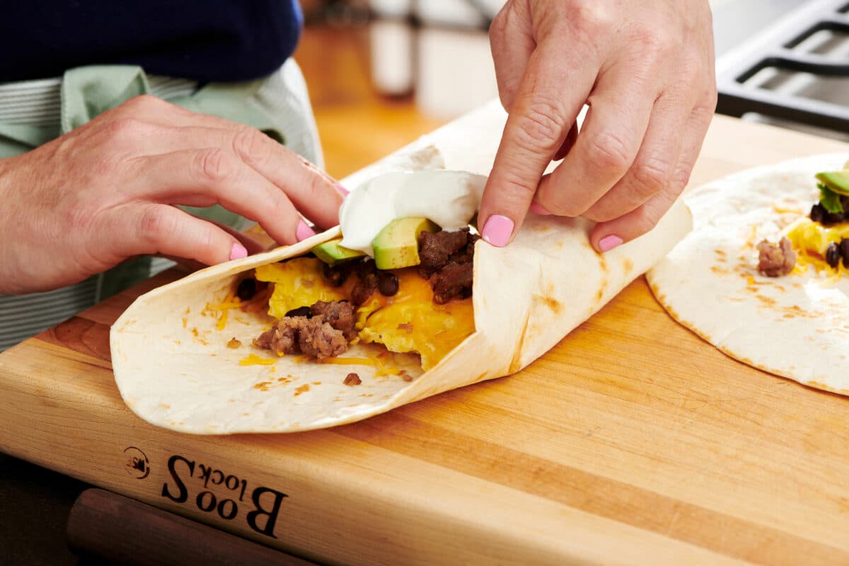 Woman folding up the sides of a tortilla filled with eggs and other ingredients.