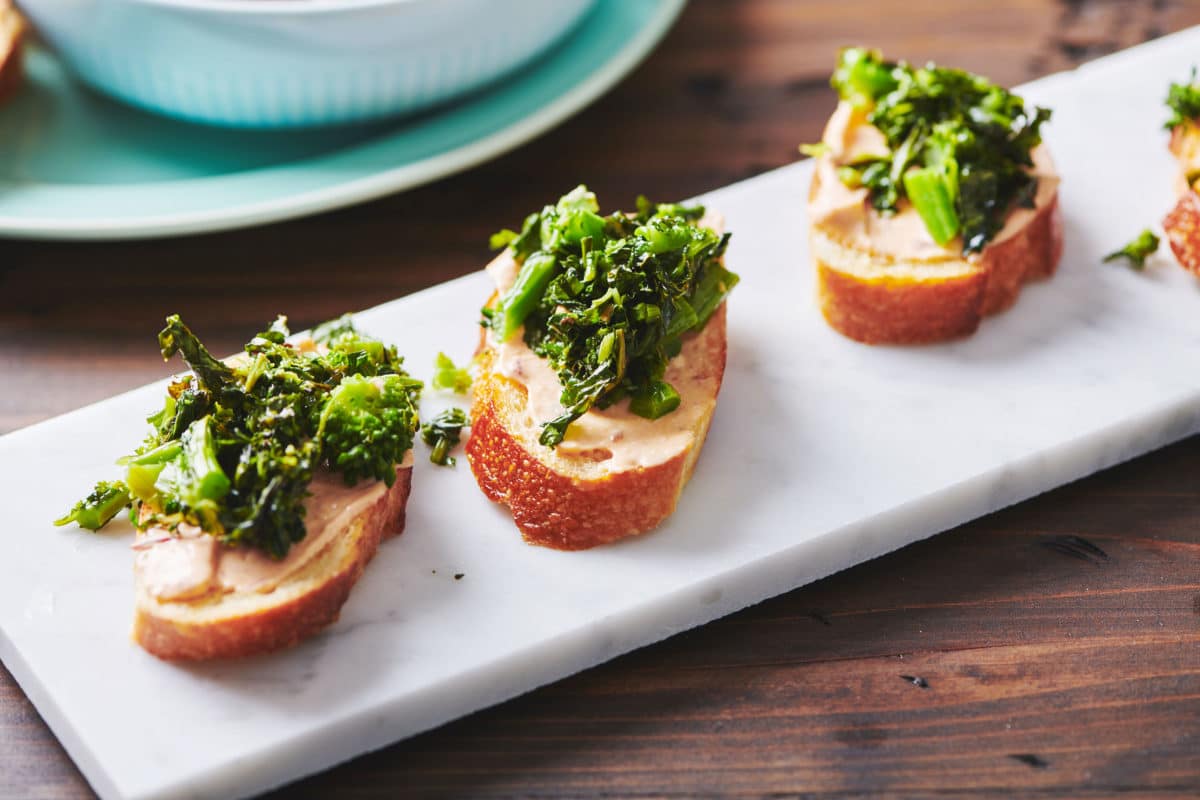 Long, white platter of Broccoli Rabe Crostini with Chipotle Sauce.