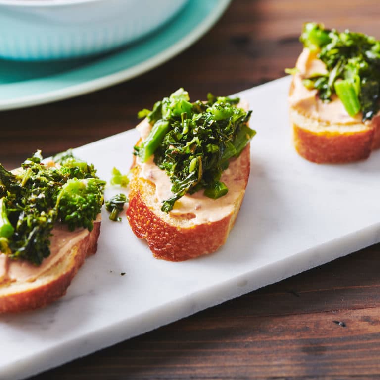 Long, white platter of Broccoli Rabe Crostini with Chipotle Sauce.