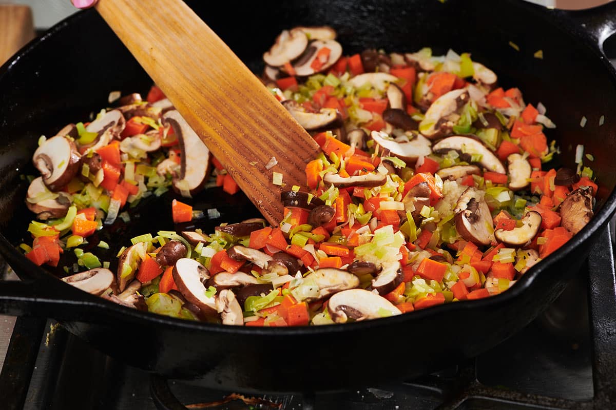 Mushrooms, leeks, carrots, and other vegetables sauteing in pan.