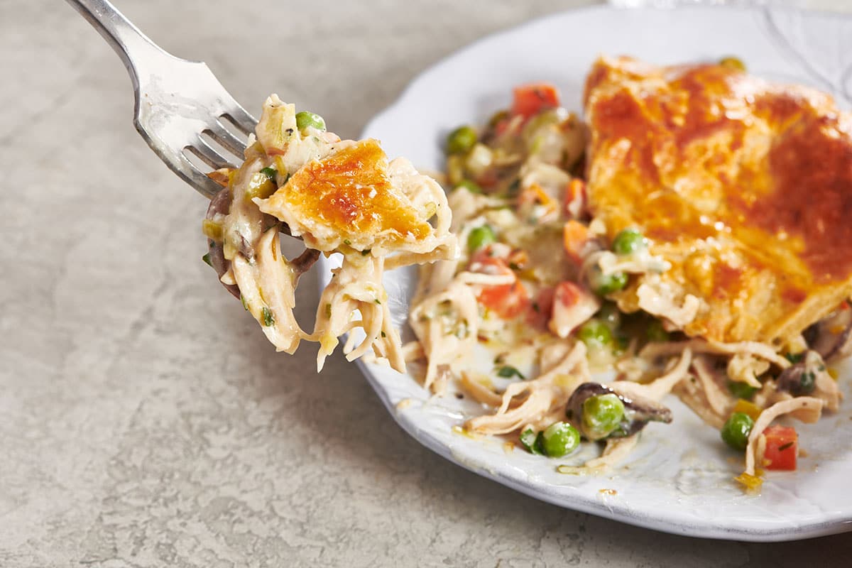 Fork serving homemade chicken pot pie over plate.
