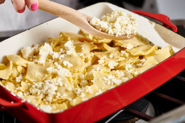 Wooden spoon placing ricotta mixture on a pan of ravioli.