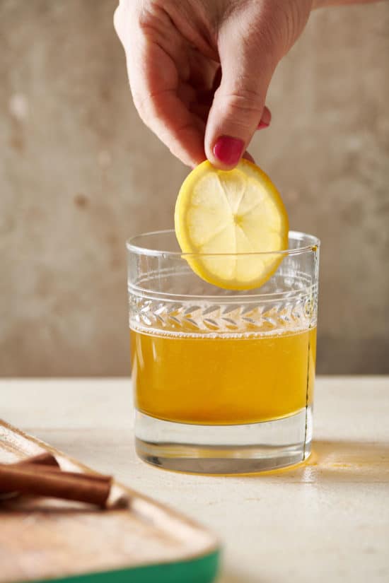 Woman placing a lemon slice into a Hot Toddy.