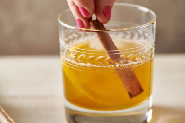 Woman placing a cinnamon stick into a Hot Toddy.