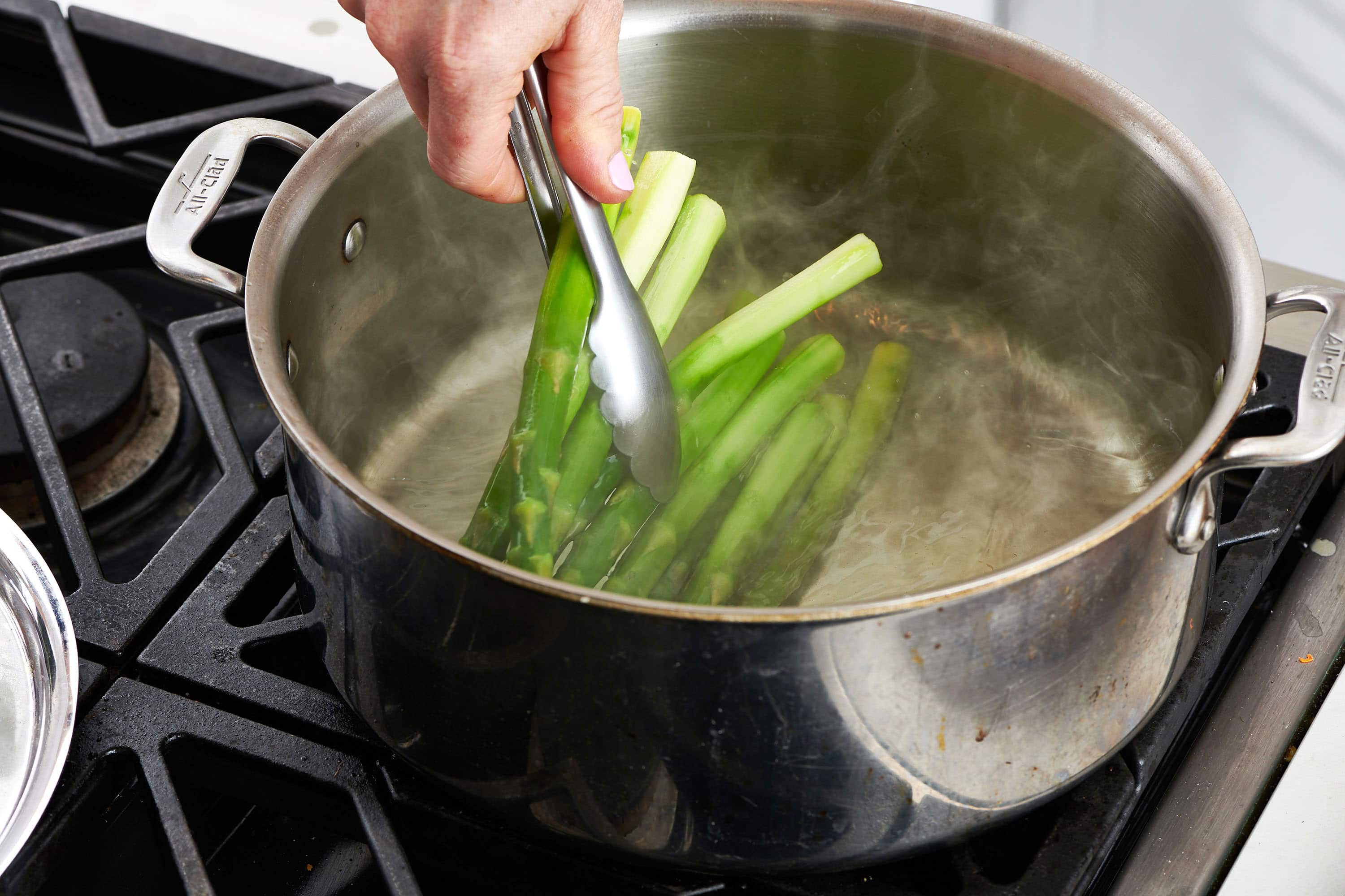 Placing raw asparagus into pot of boiling water with tongs.