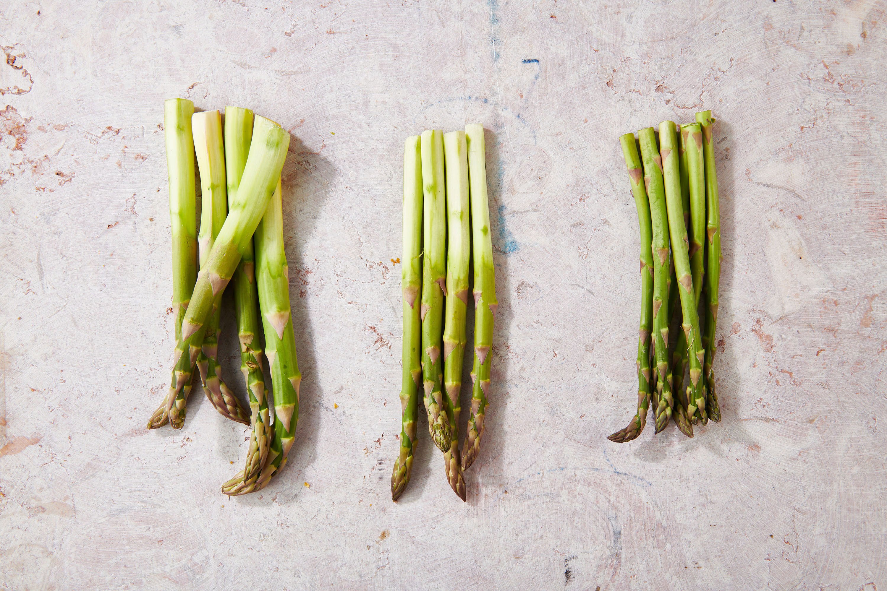 Thick, medium, and thin fresh asparagus spears on table.