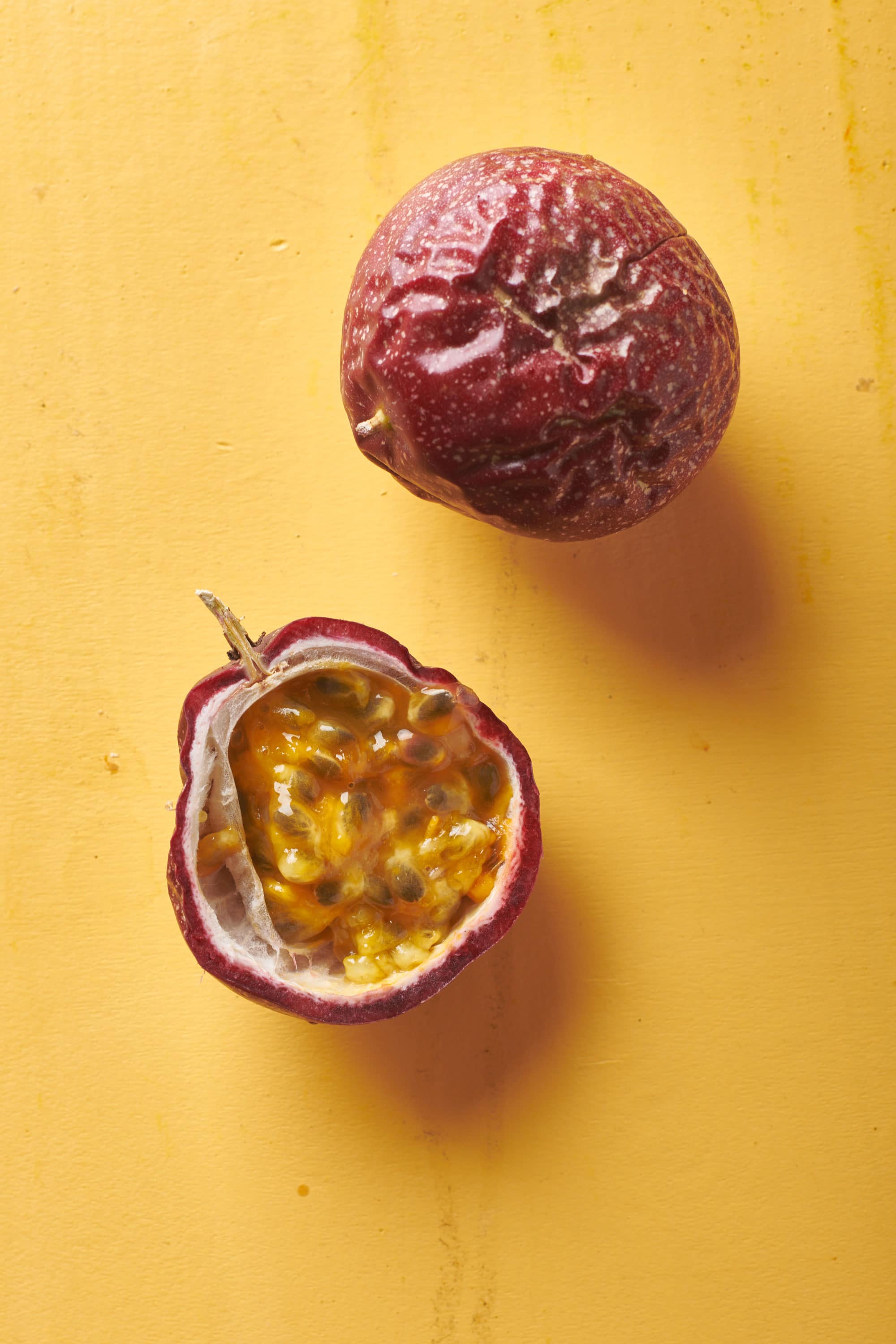 Two ripe passion fruits on a yellow surface.