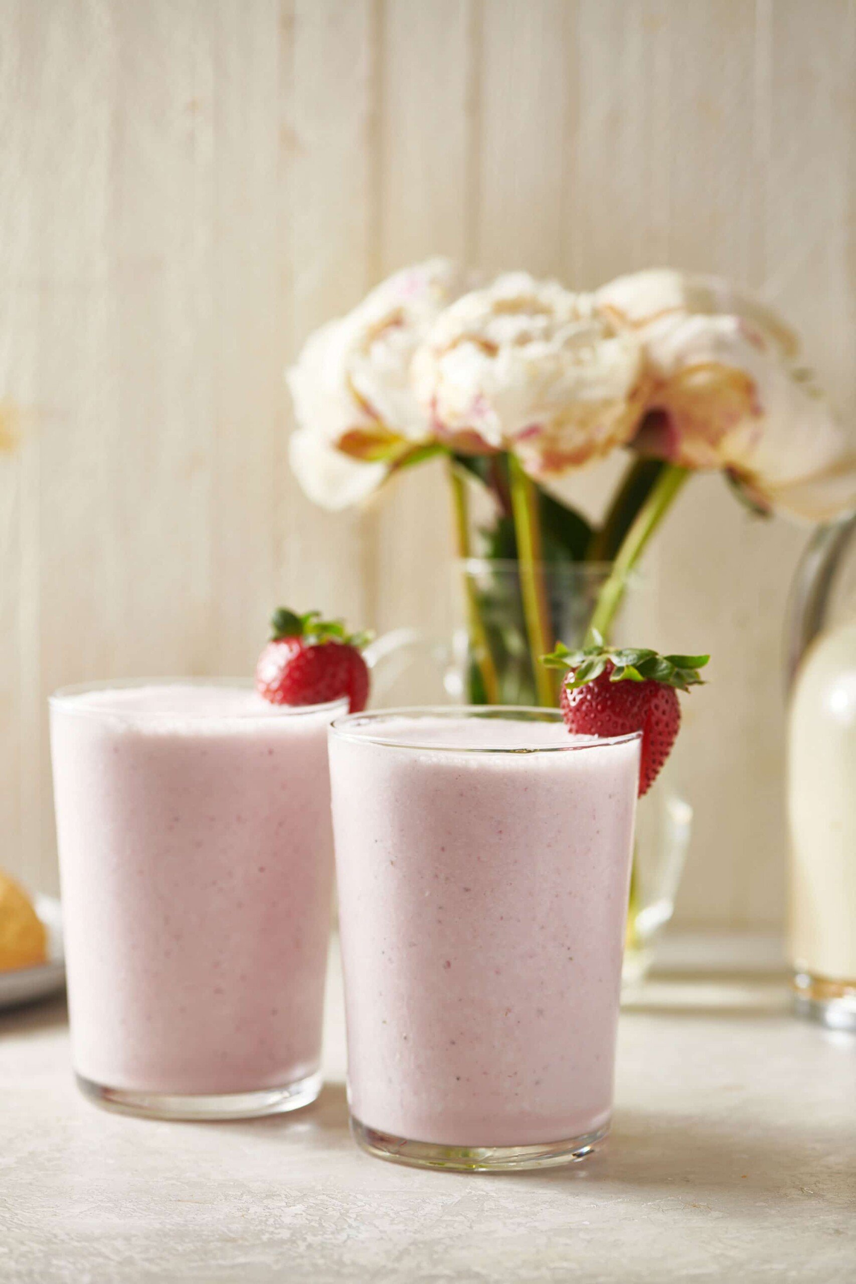 Two strawberry milkshakes on table with white flowers.