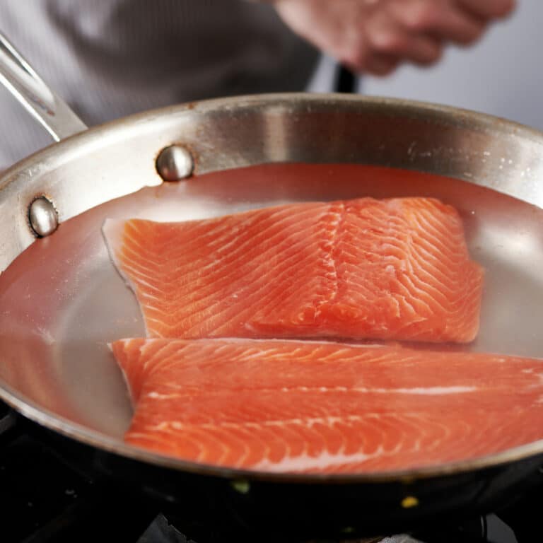 Poaching salmon filets in pan on stovetop.