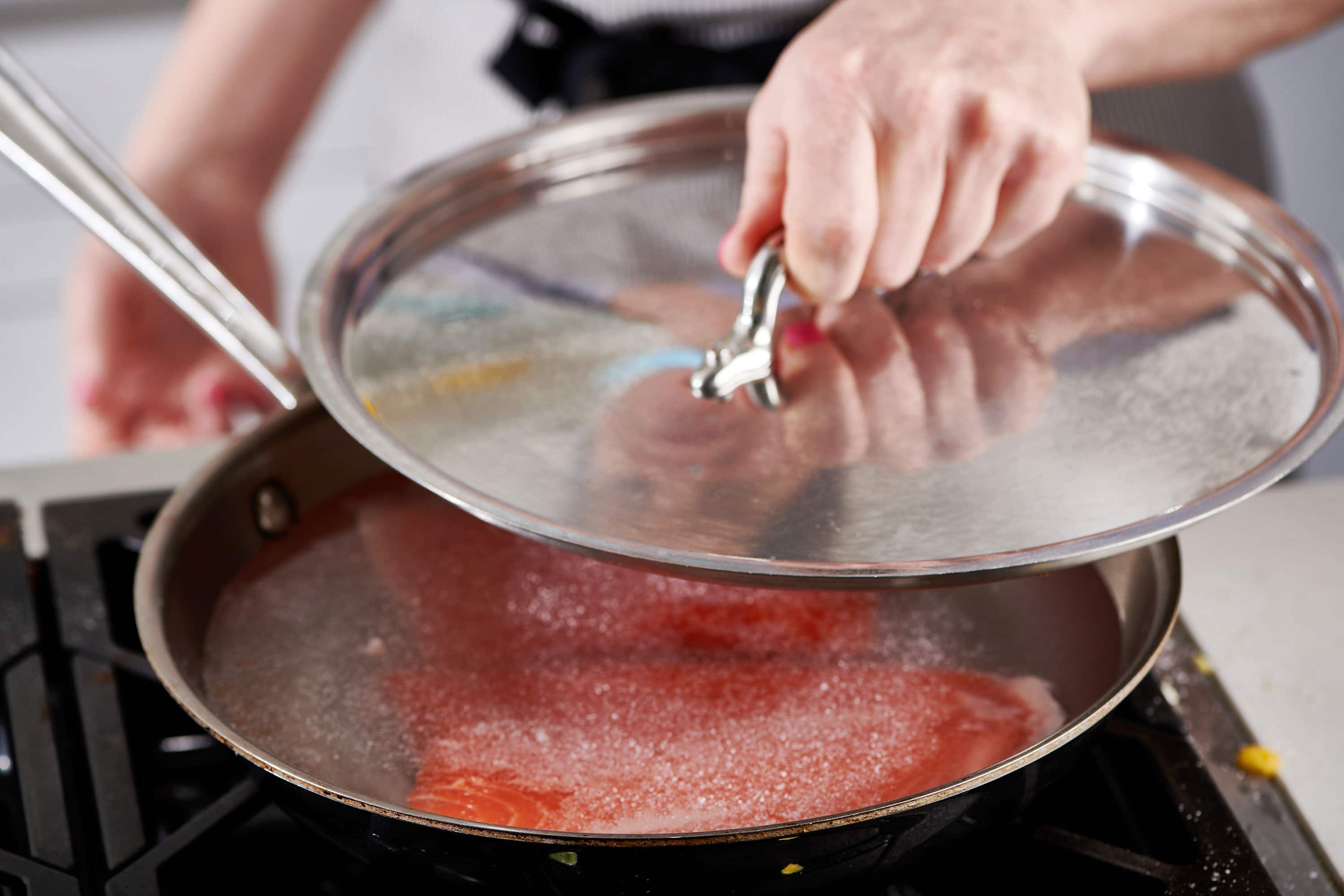 Woman putting a lid onto a skillet with water, salt, and salmon.