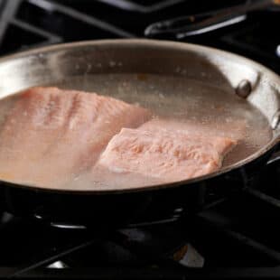 Salmon in a skillet of water on a stovetop.