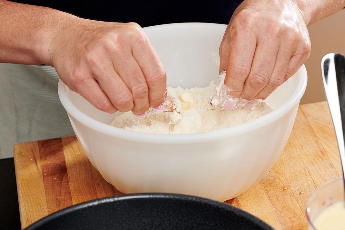 Woman rubbing chilled butter into a bowl of flour mixture.