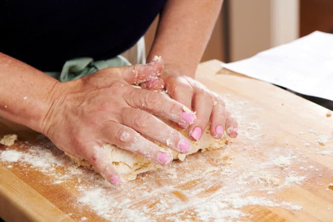 Woman kneading dough on a wooden board.