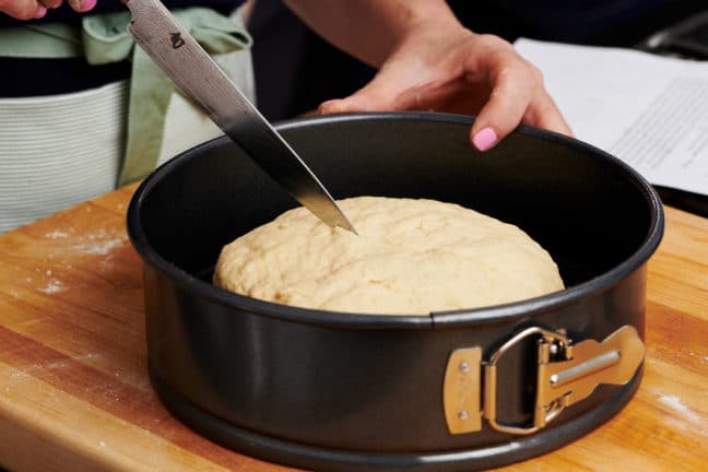 Woman scoring bread dough with a large knife.