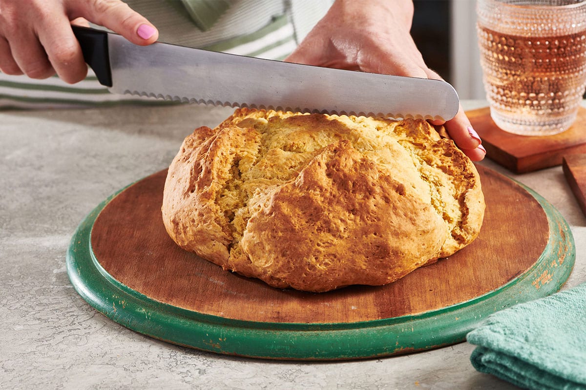 Woman cutting a loaf of Irish Soda Bread with a bread knife.