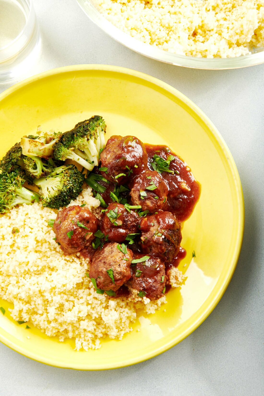 Sweet and Sour Meatballs on a plate with broccoli and couscous.