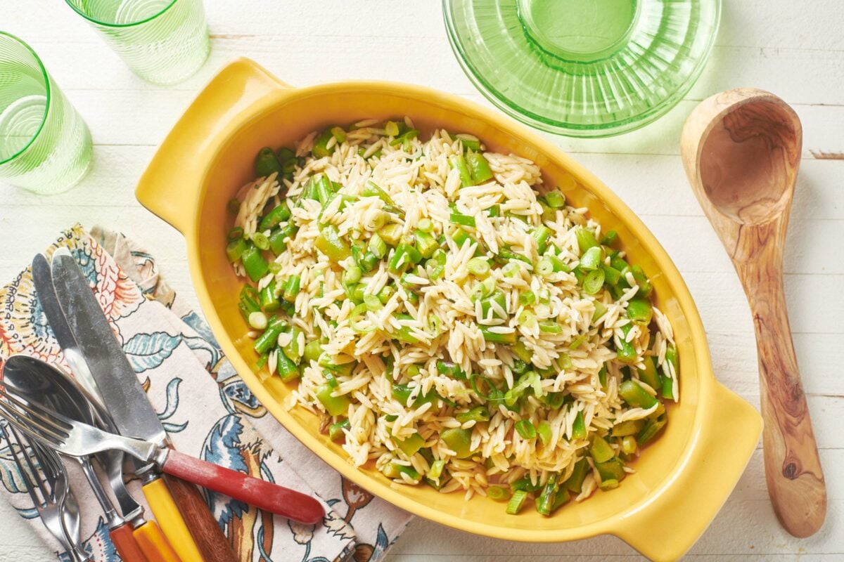 Salad of orzo, asparagus, and peas in a yellow serving dish.