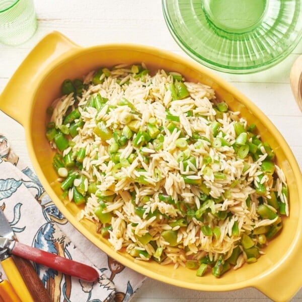 Salad of orzo, asparagus, and peas in a yellow serving dish.