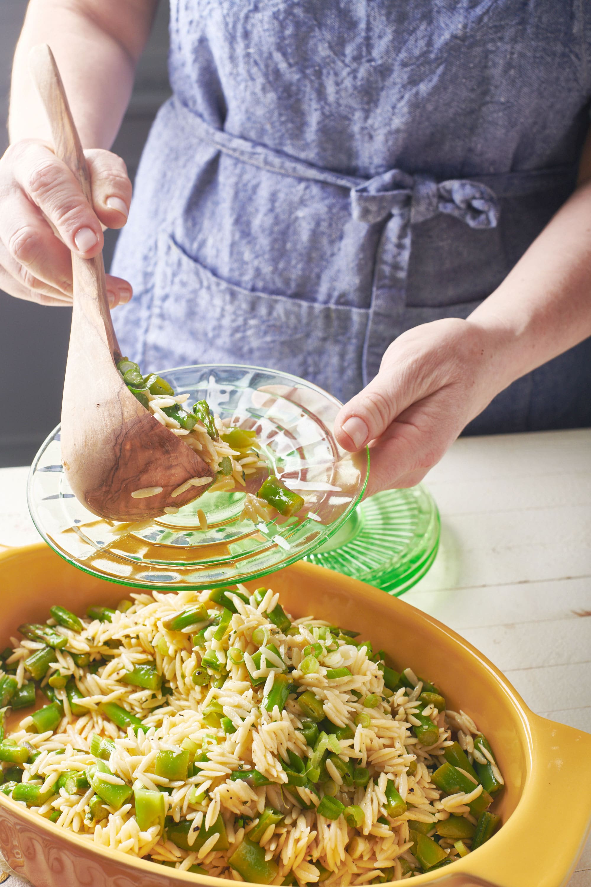 Woman scooping Vegetarian Spring Orzo Salad onto a glass plate.