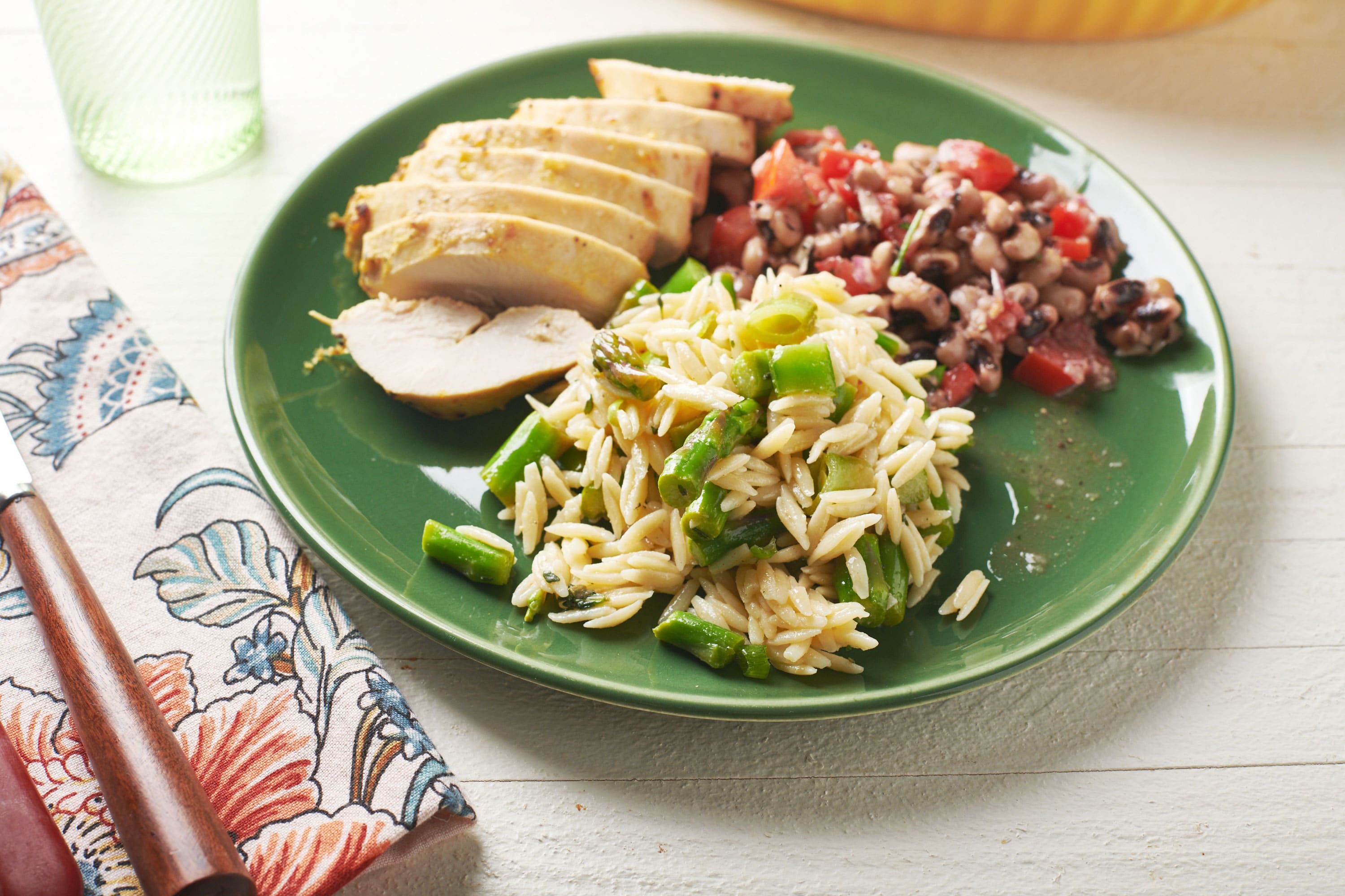 Green plate with Vegetarian Spring Orzo Salad, meat, and beans.