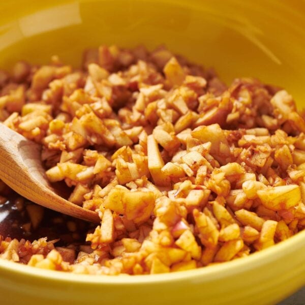 Homemade charoset in yellow bowl with wood spoon.