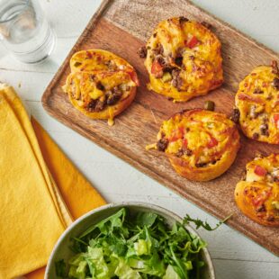 Cheeseburger Pizza Pinwheels on a wooden board with a bowl of salad.