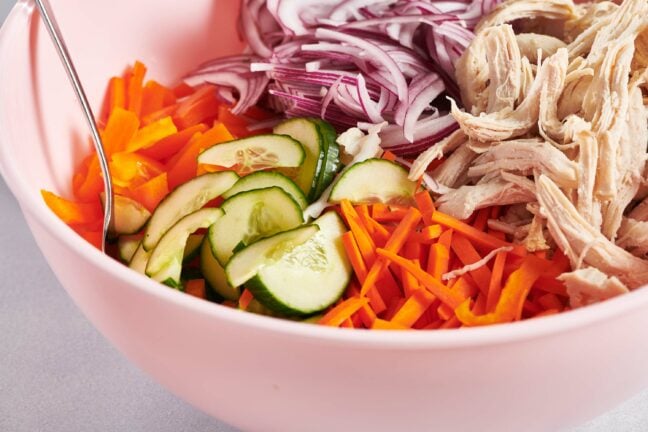 Ingredients for Chinese Chicken Salad, including red onion and chicken, unmixed in a bowl.