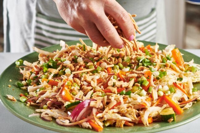 Woman sprinkling lo mein over a Chinese Chicken Salad.