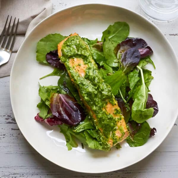 Salmon with herb sauce over salad on white plate.