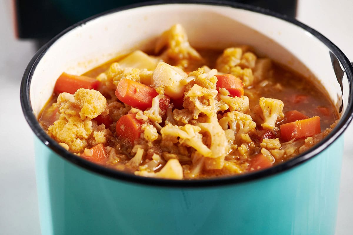 Cauliflower and carrots with broth simmering in turquoise soup pot.