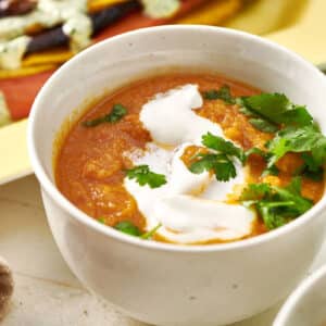 Moroccan Carrot and Cauliflower Soup in white bowl on table with sour cream and parsley.