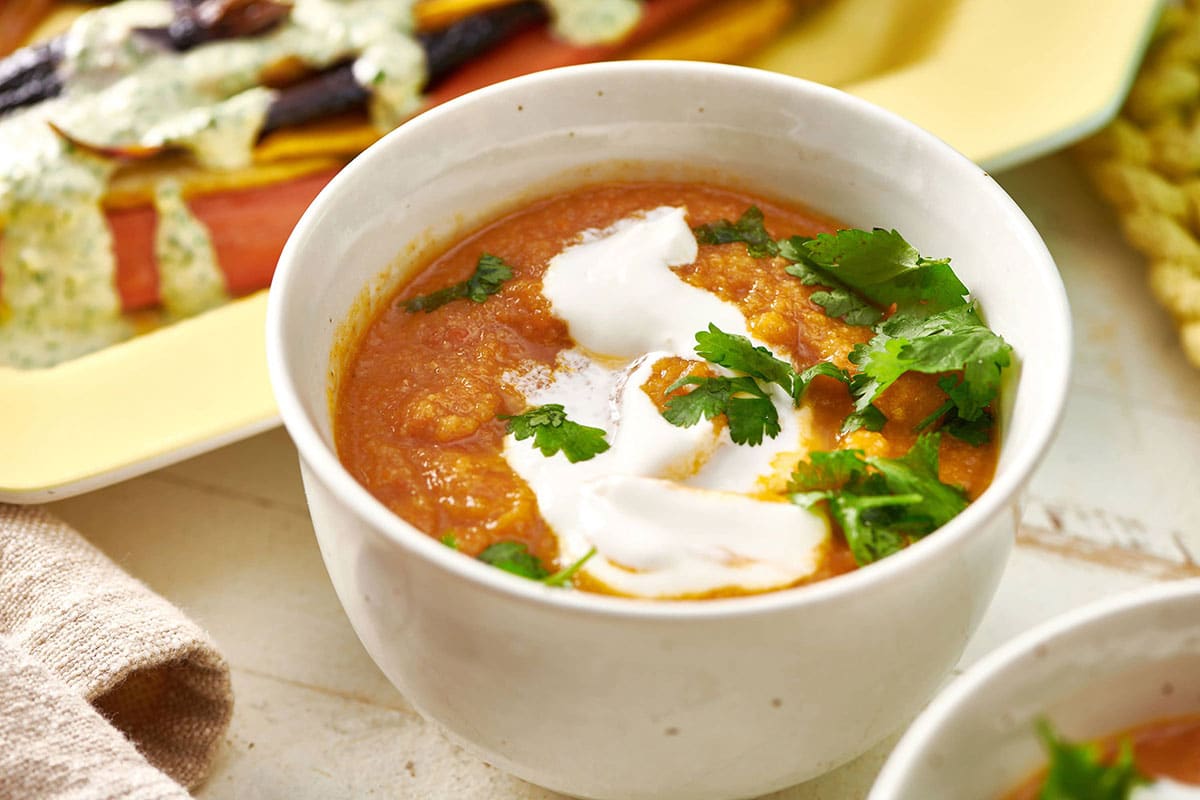Moroccan Carrot and Cauliflower Soup in white bowl on table with sour cream and parsley.
