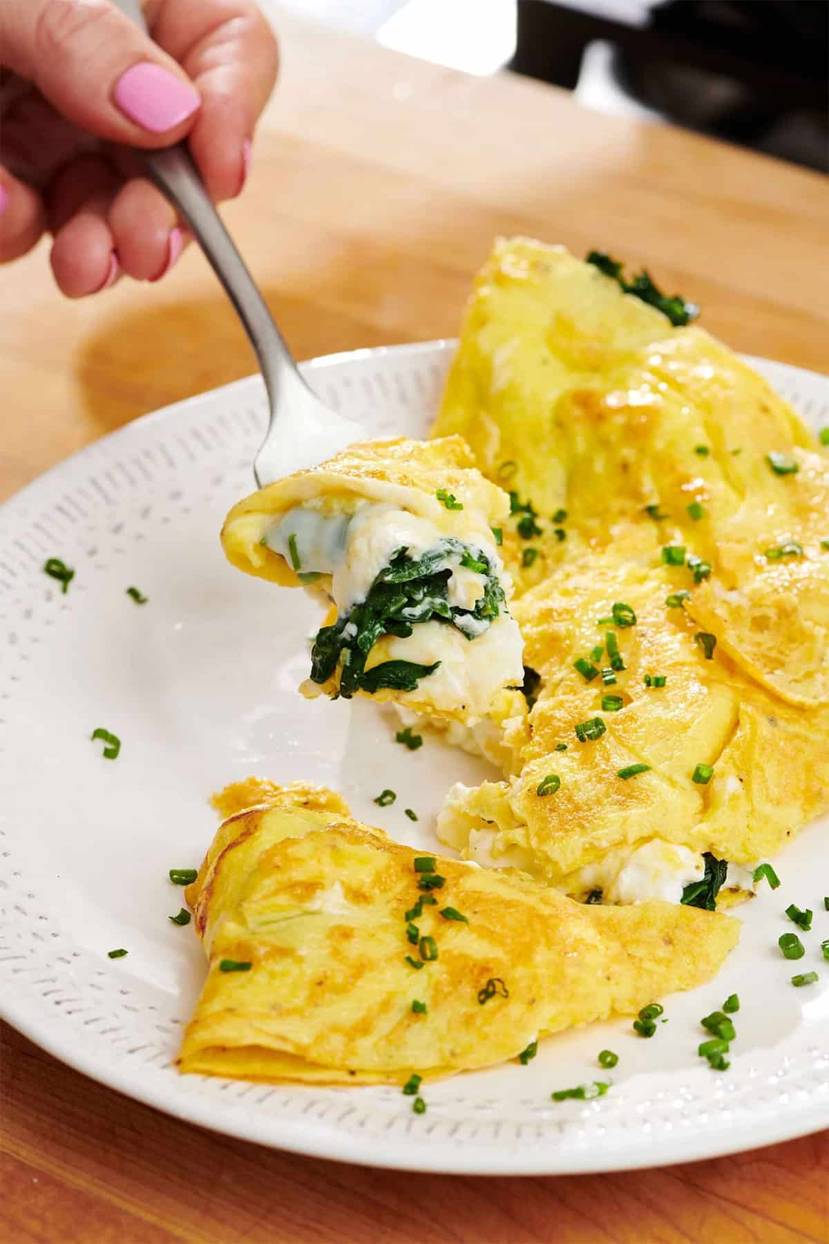 Eating spinach and feta omelet with fresh chives using a fork.