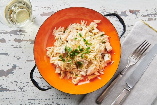 Chicken Piccata Orzo Salad in an orange bowl on a white, wooden table.