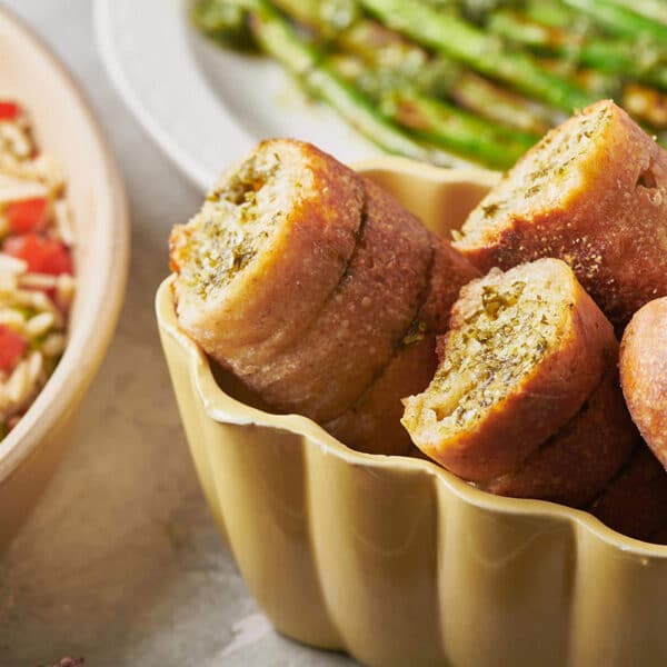 Sliced garlic bread with chimichurri sauce in bowl on table.