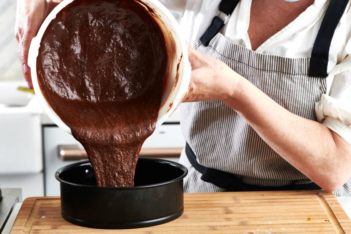 Woman pouring chocolate cake batter into a pan.