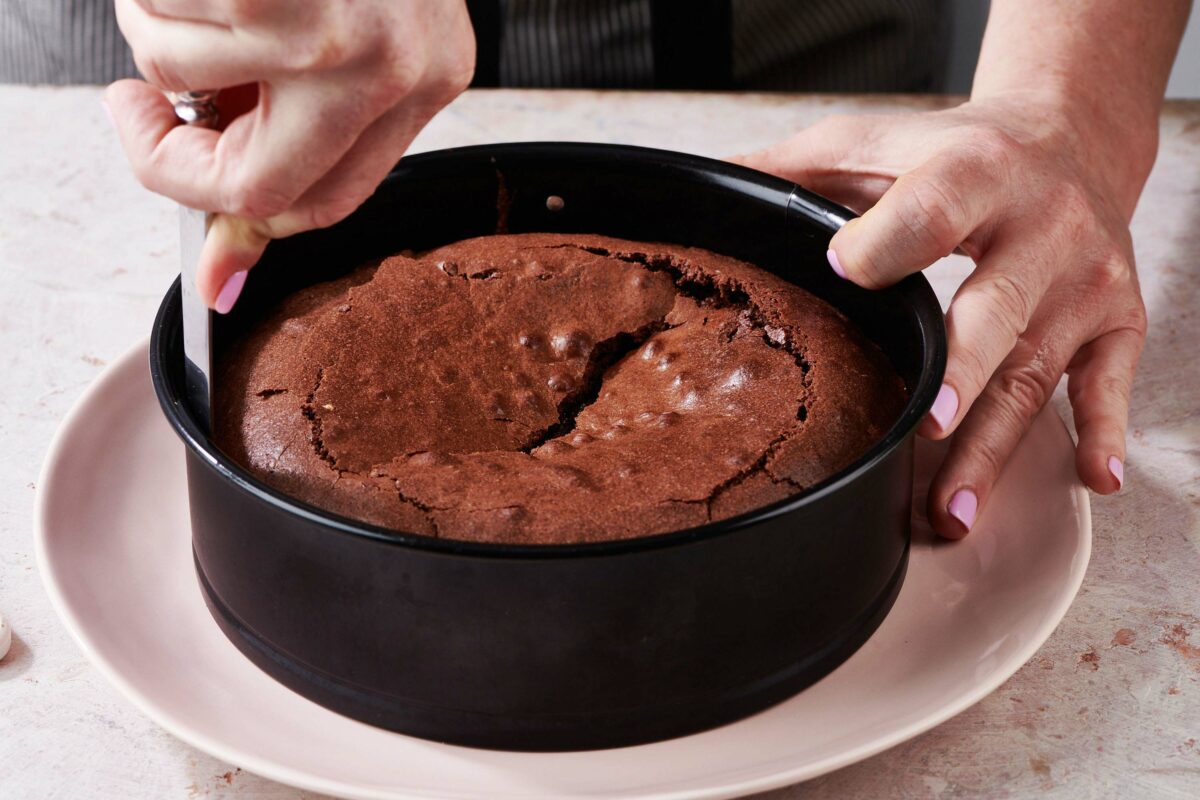 Woman running a knife around the inside edge of a springform pan of chocolate cake.