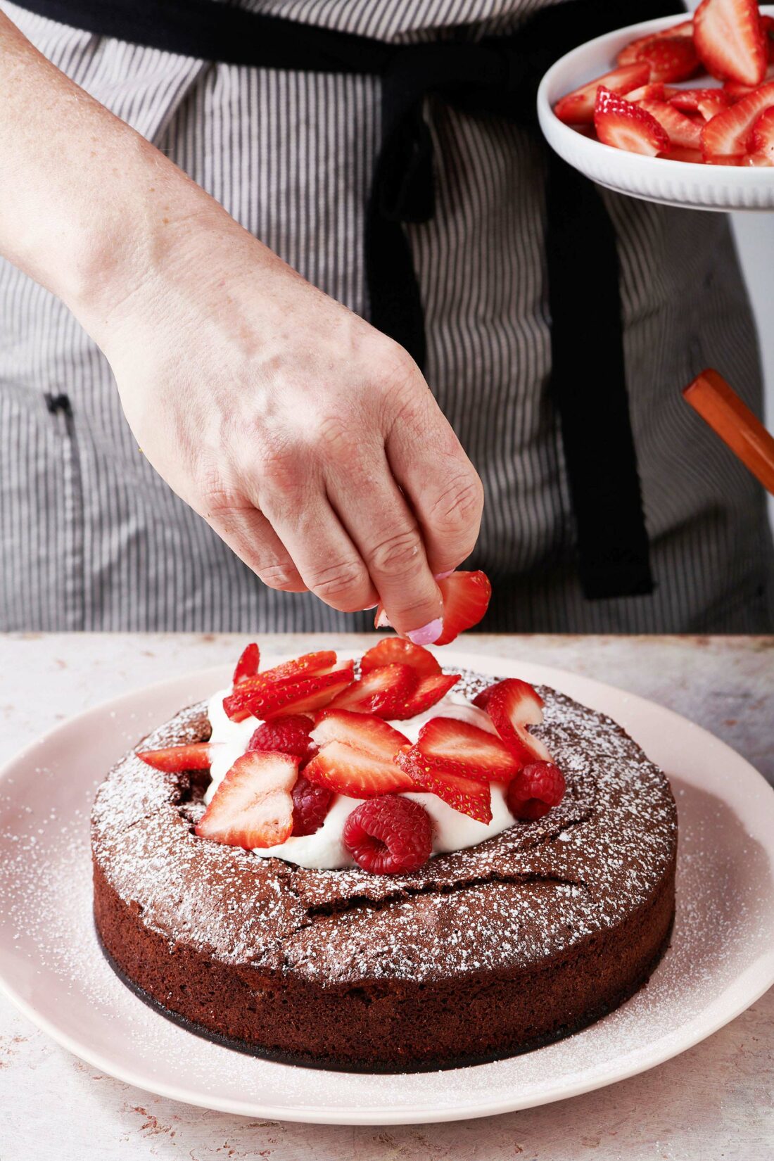 Woman adding sliced strawberries to the top of a Fudgy Chocolate Cake.