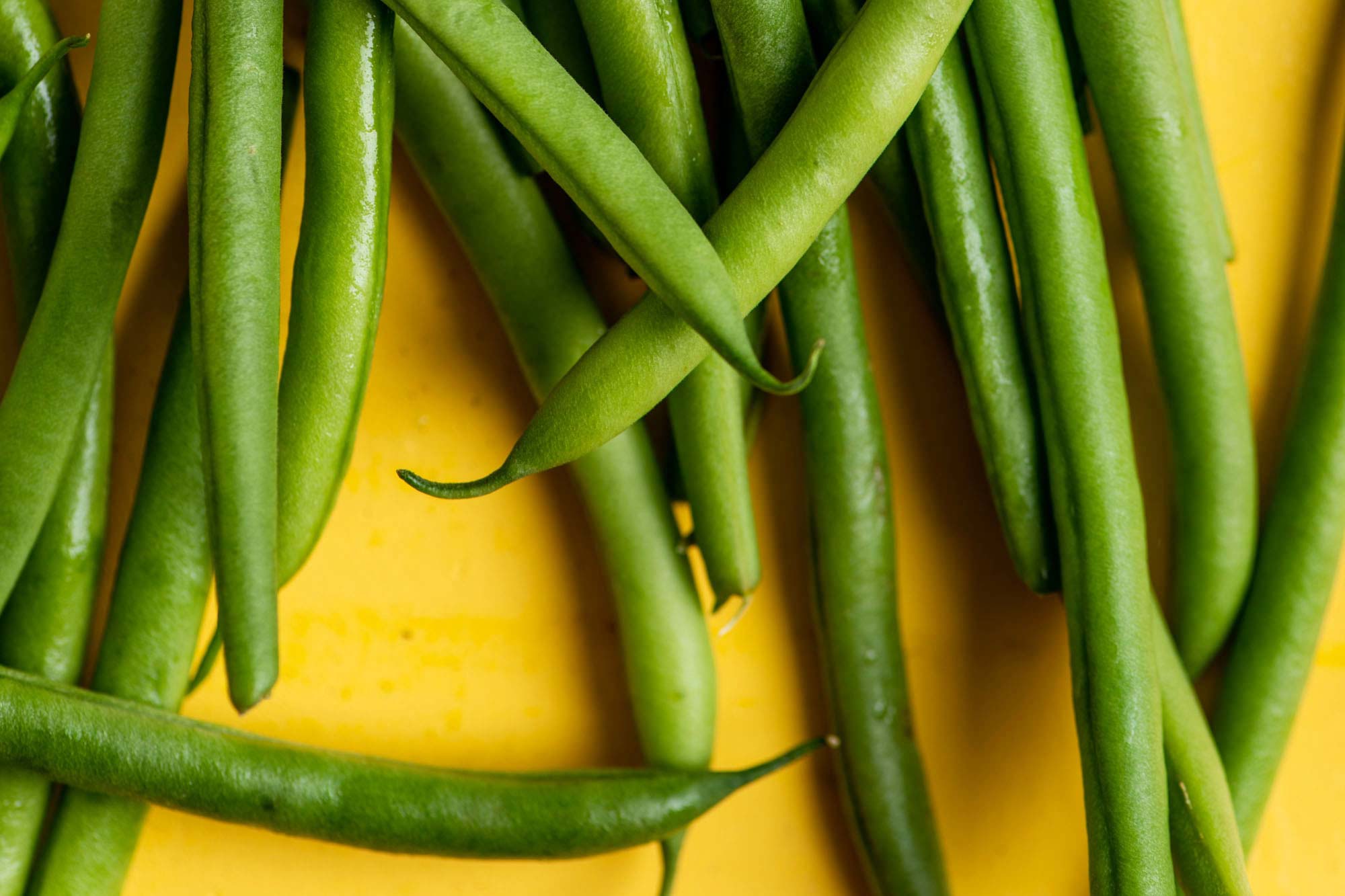 Whole Haricot Verts on a yellow surface.