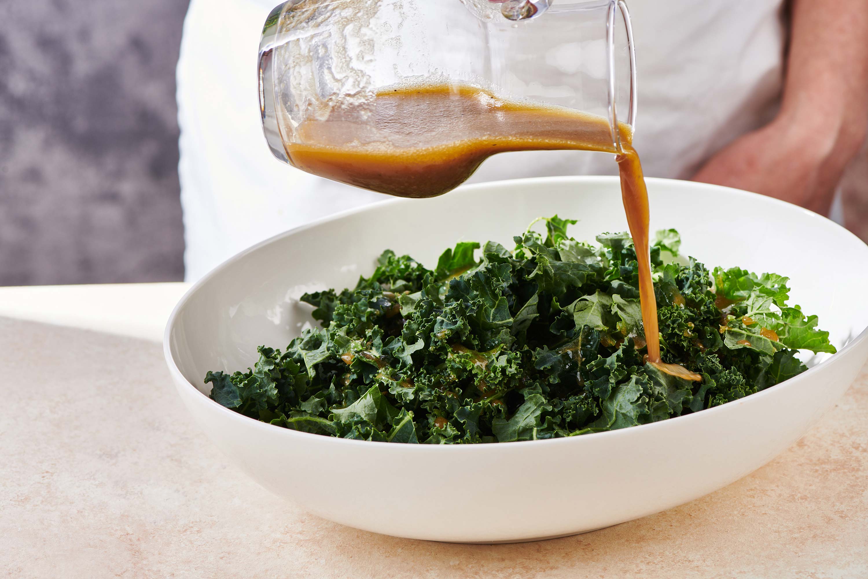 Apple Dijon dressing pouring over a bowl of kale.