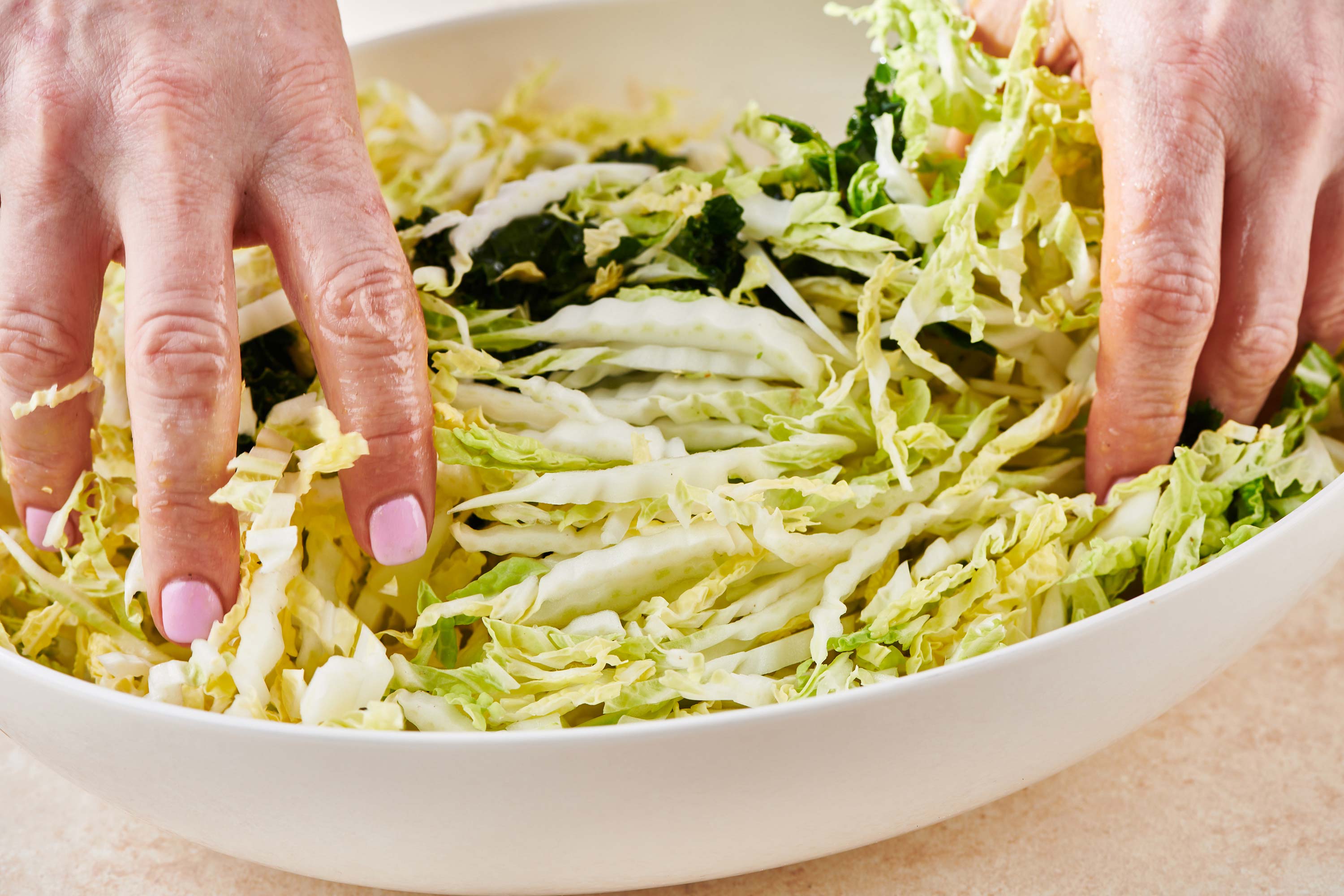 Woman tossing cabbage in a bowl of kale and dressing.