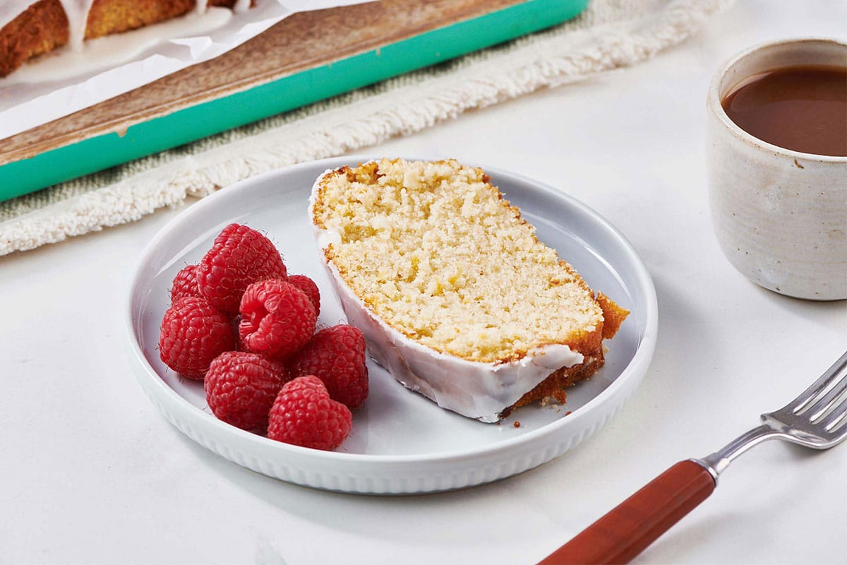 Slice of glazed lemon cake on plate with raspberries.