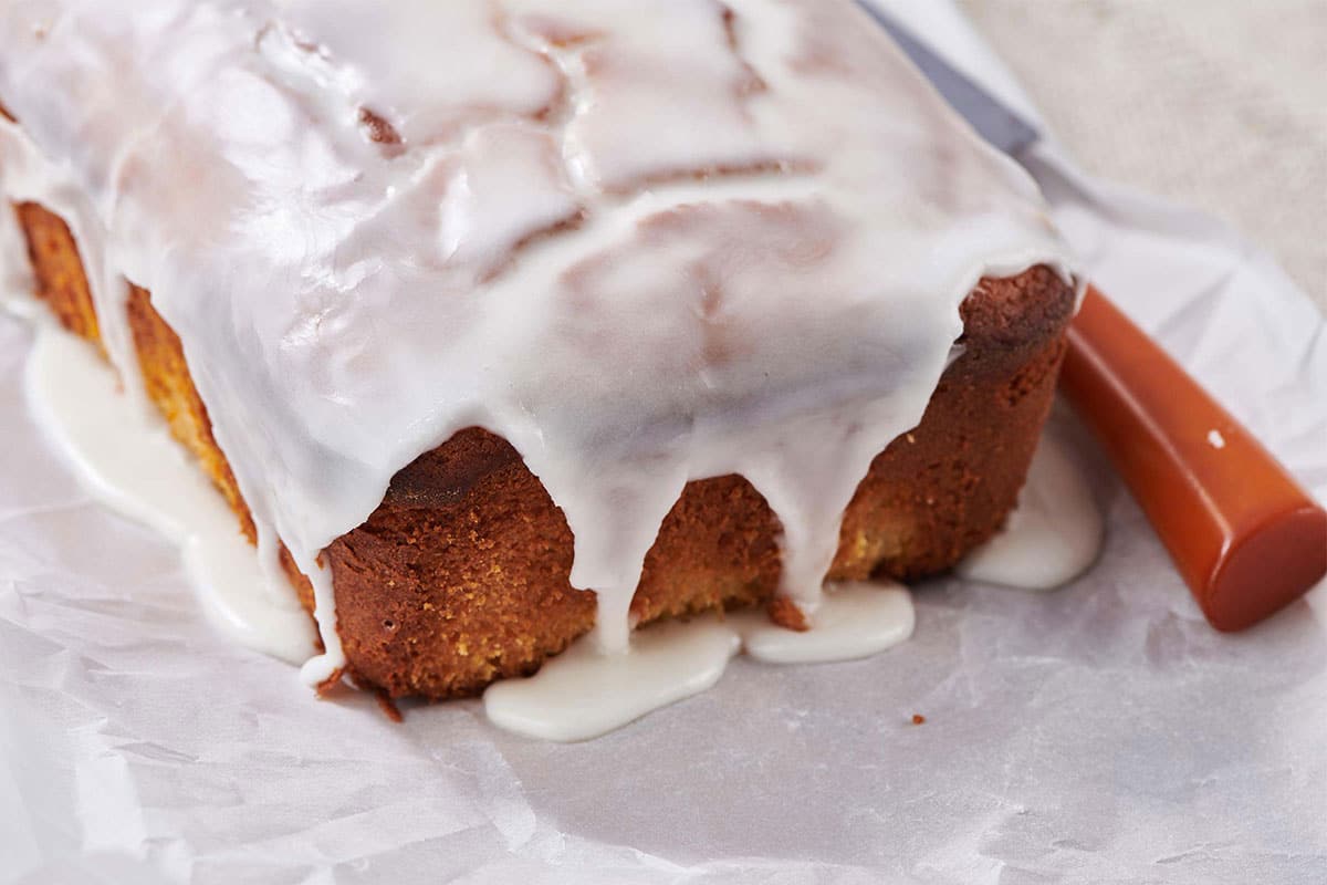 Glaze running over lemon cake on parchment paper.
