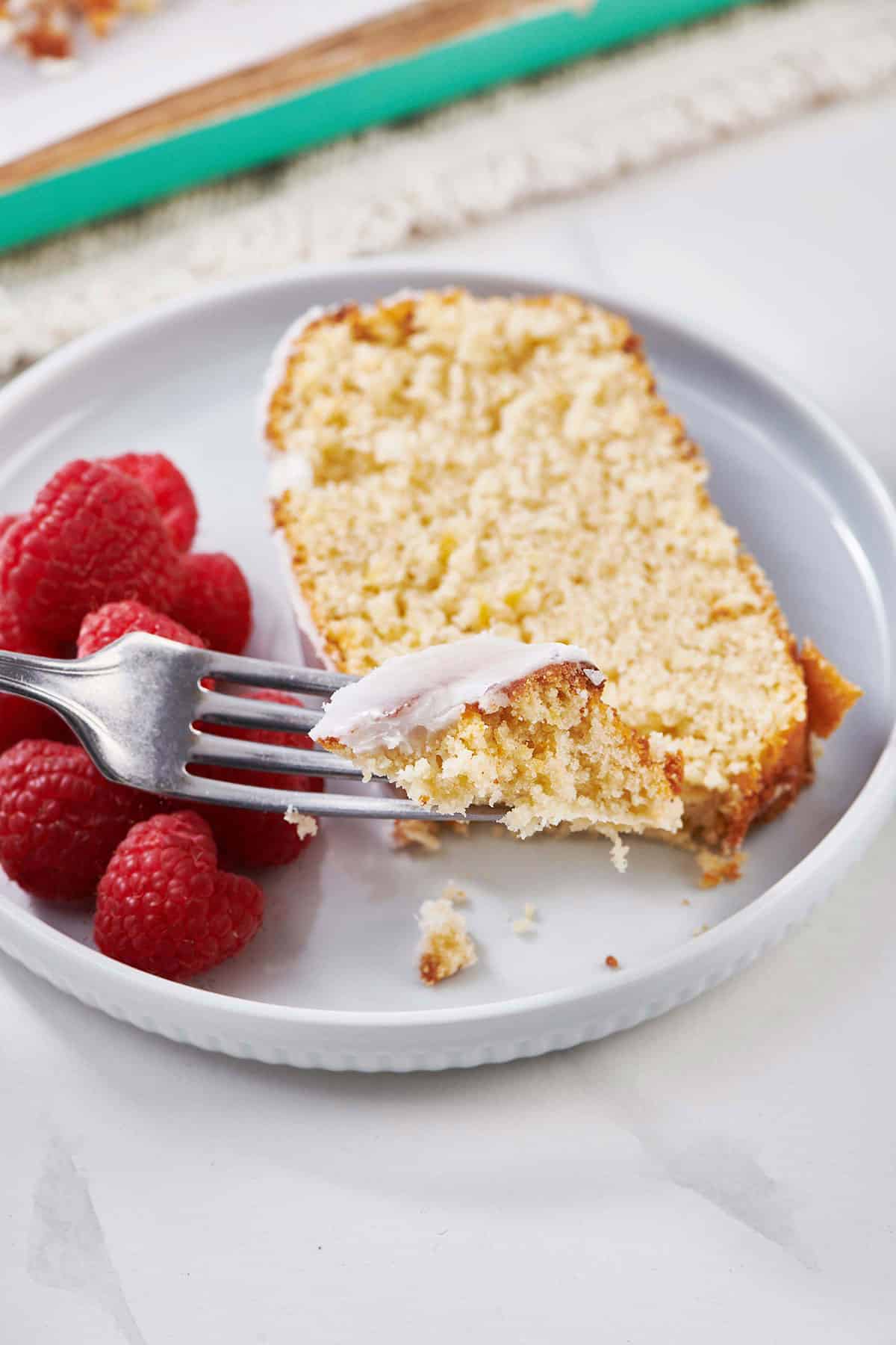 Eating glazed lemon cake and raspberries with fork.
