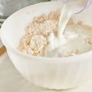 Buttermilk pouring into a bowl of flour mixture.