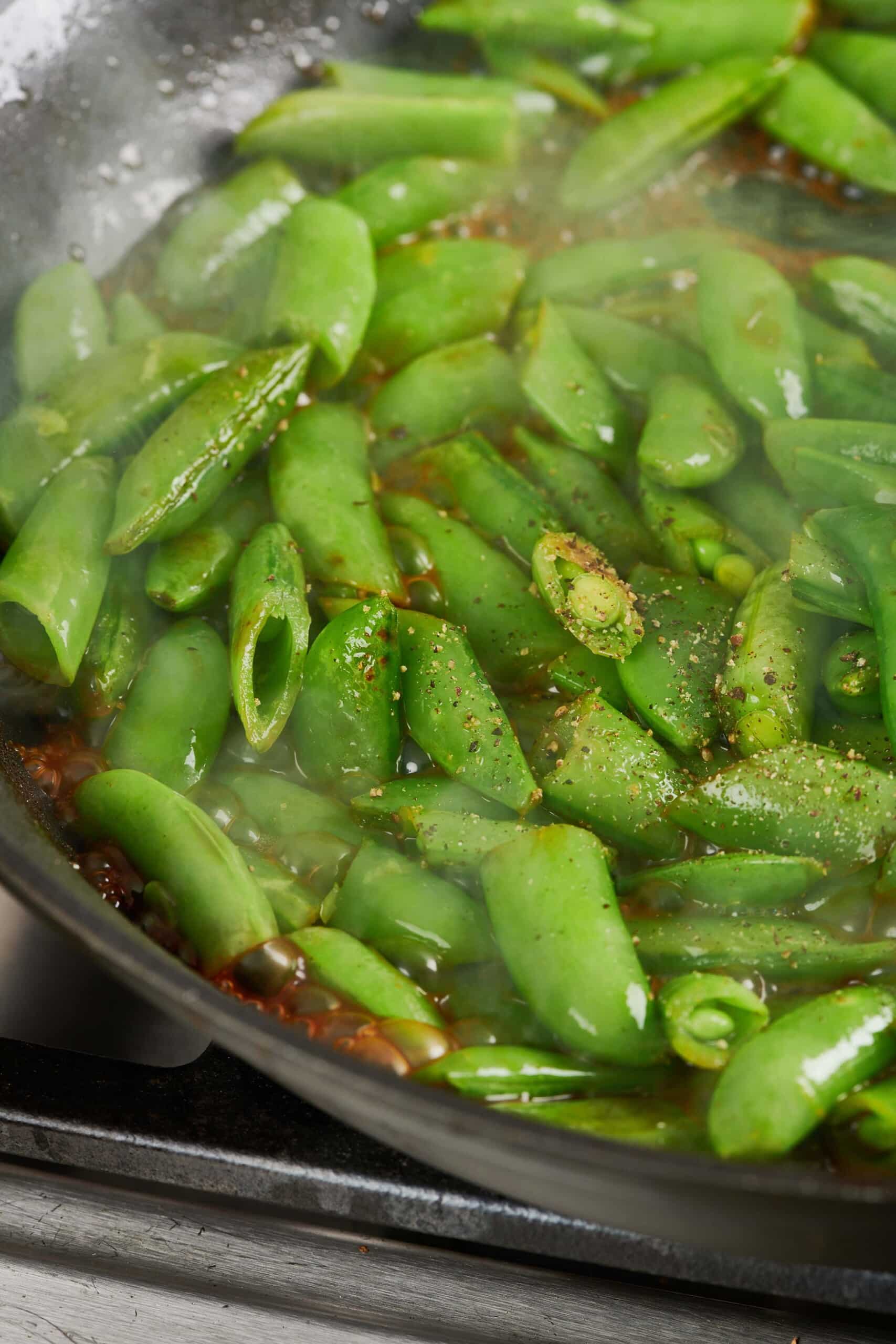 Soy Glazed Sugar Snap Peas sti-fried in pan with pepper.