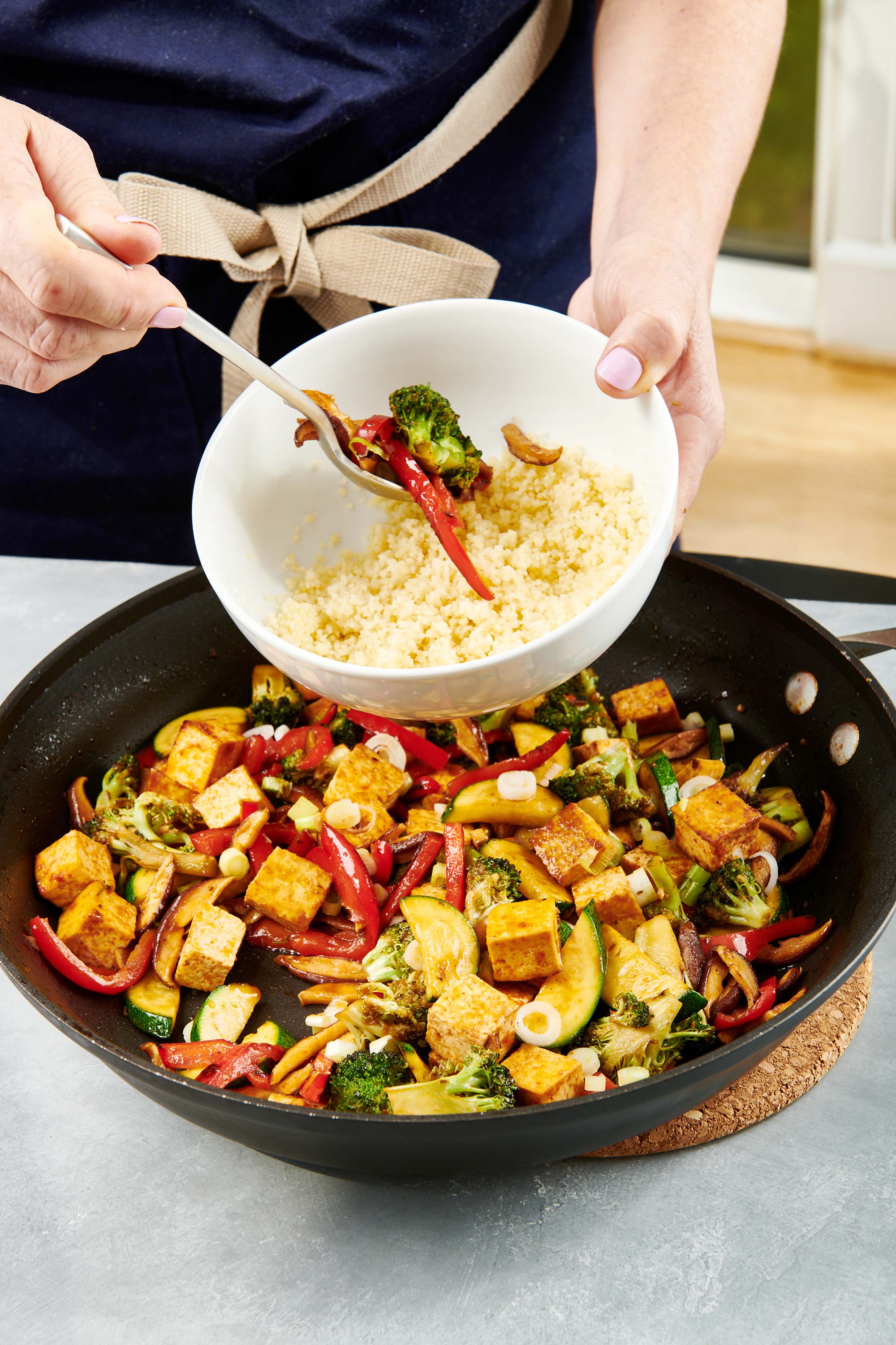 Woman putting Stir Fried Crispy Tofu and Vegetables into a bowl of rice.