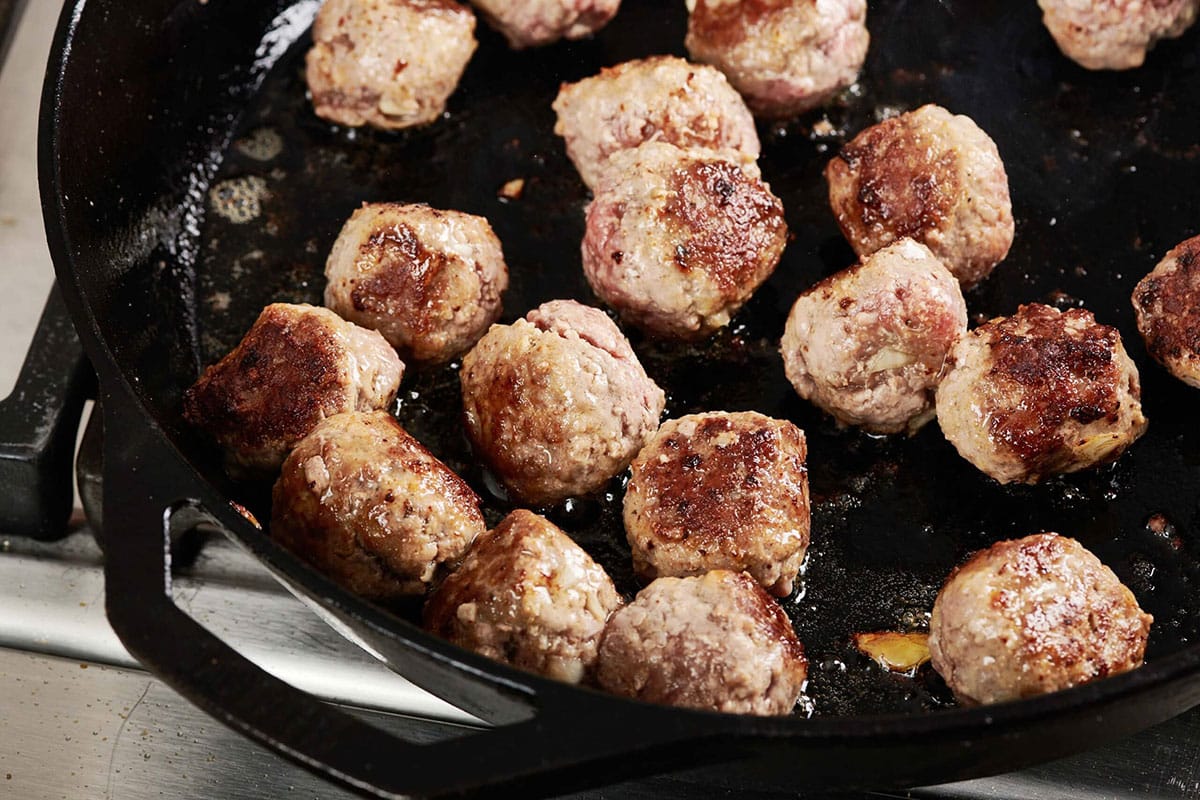 Meatballs cooking in cast-iron skillet.