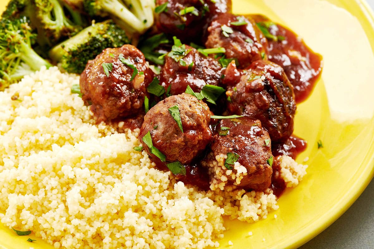 Sweet and sour meatballs on yellow plate with rice and broccoli.