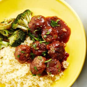 Sweet and sour meatballs over rice on yellow plate.